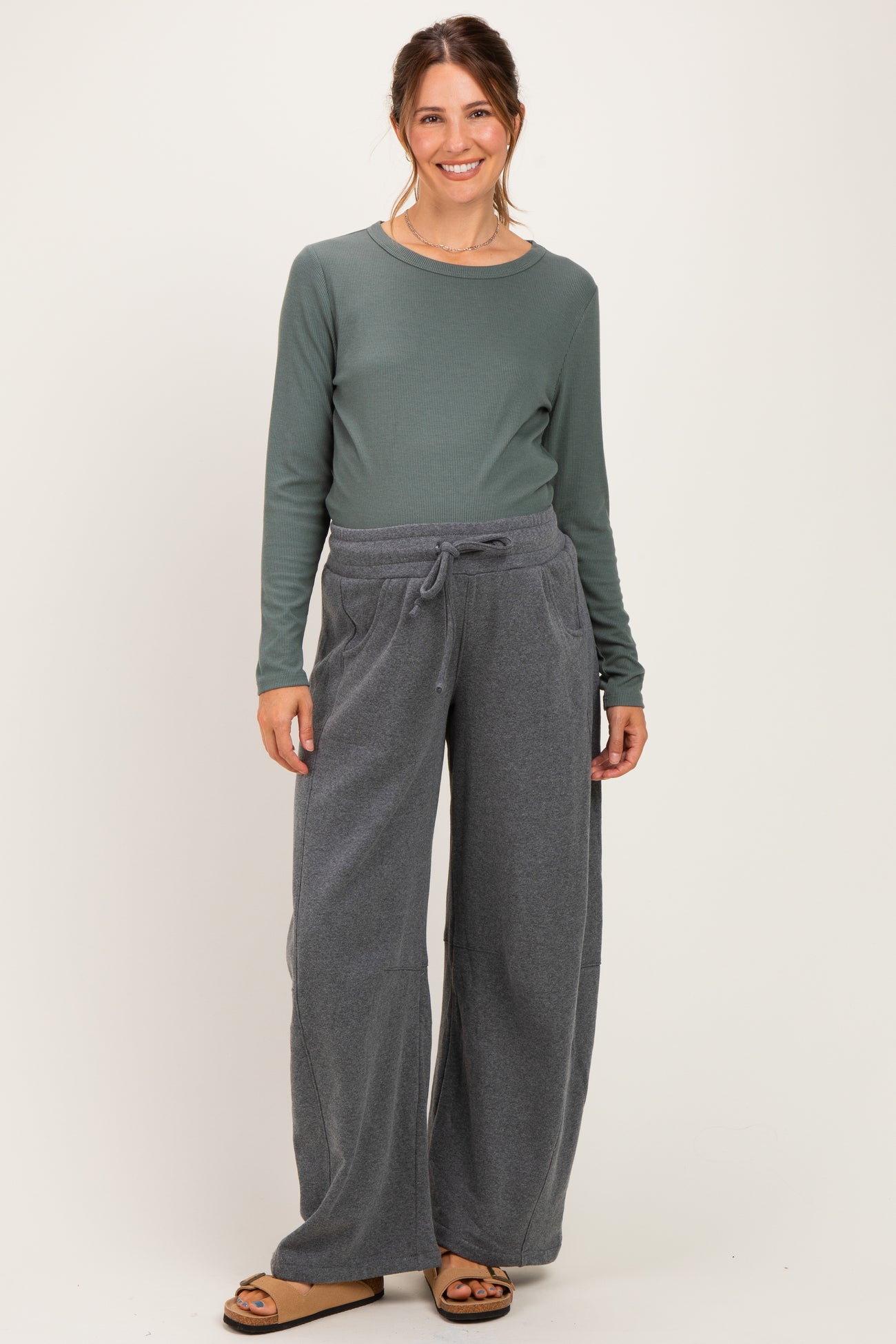 woman wearing a green long sleeve ribbed maternity top and gray wide-leg maternity sweatpants, smiling