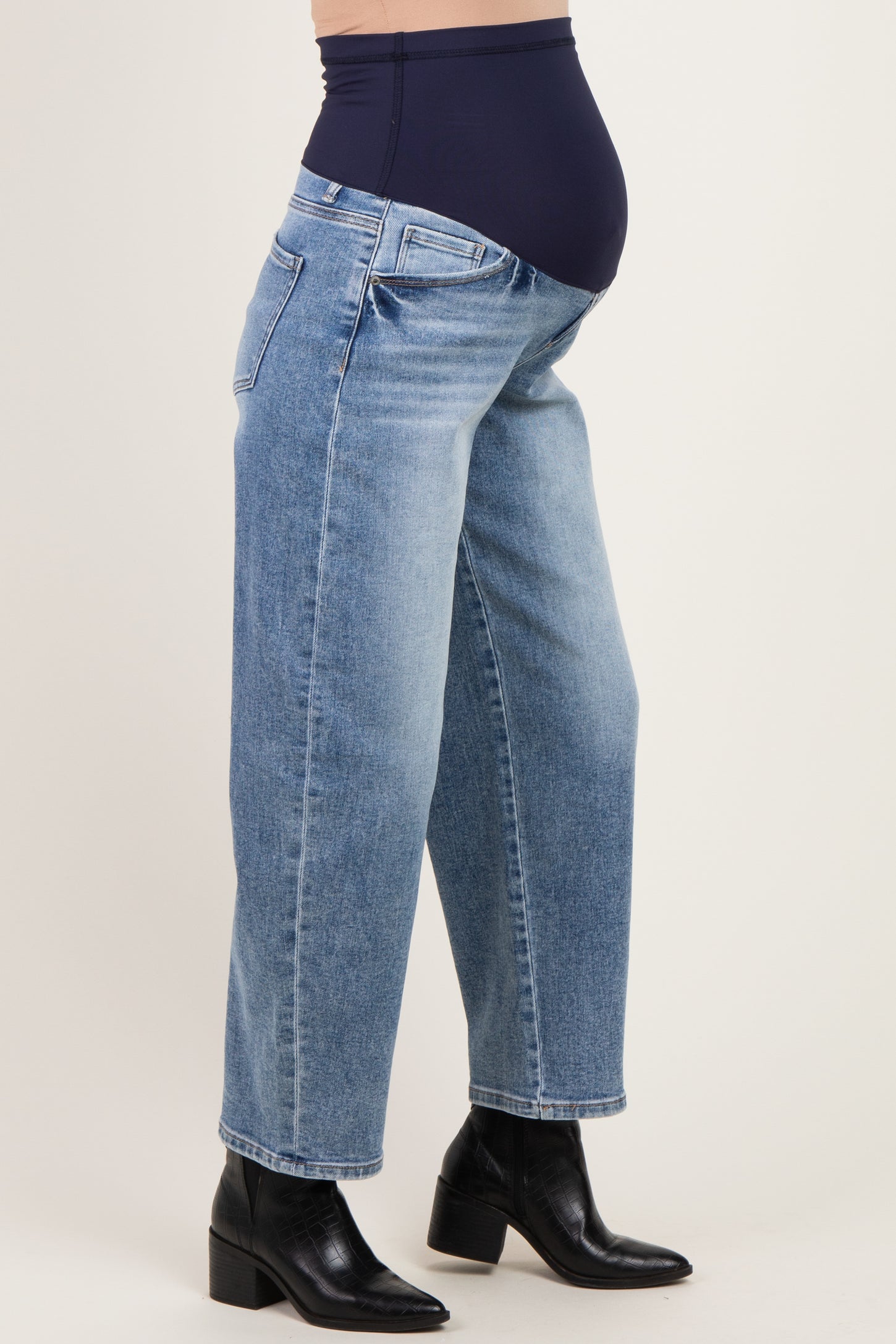 woman wearing light blue maternity jeans with a dark blue over-the-bump waistband and black ankle boots, showing a baby bump