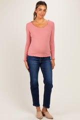 woman wearing a pink long sleeve maternity top with a scalloped neckline and a visible baby bump paired with dark blue jeans