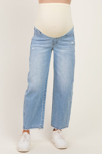 woman wearing light blue maternity jeans with a supportive beige belly band, styled with white sneakers