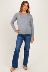 woman wearing a light gray long sleeve maternity sweater and blue flared jeans, with a subtle baby bump visible
