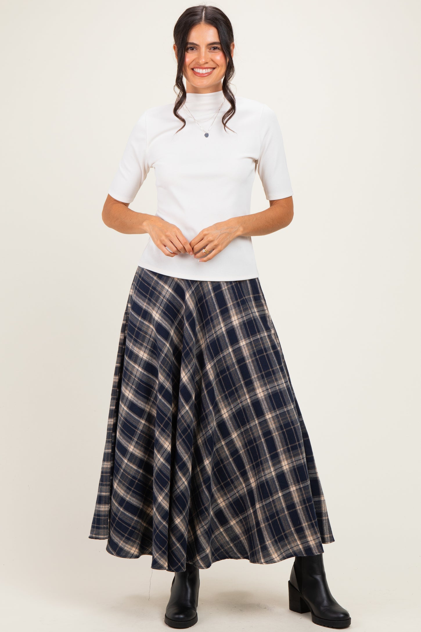 woman wearing a white short sleeve top and a long navy plaid skirt with black boots