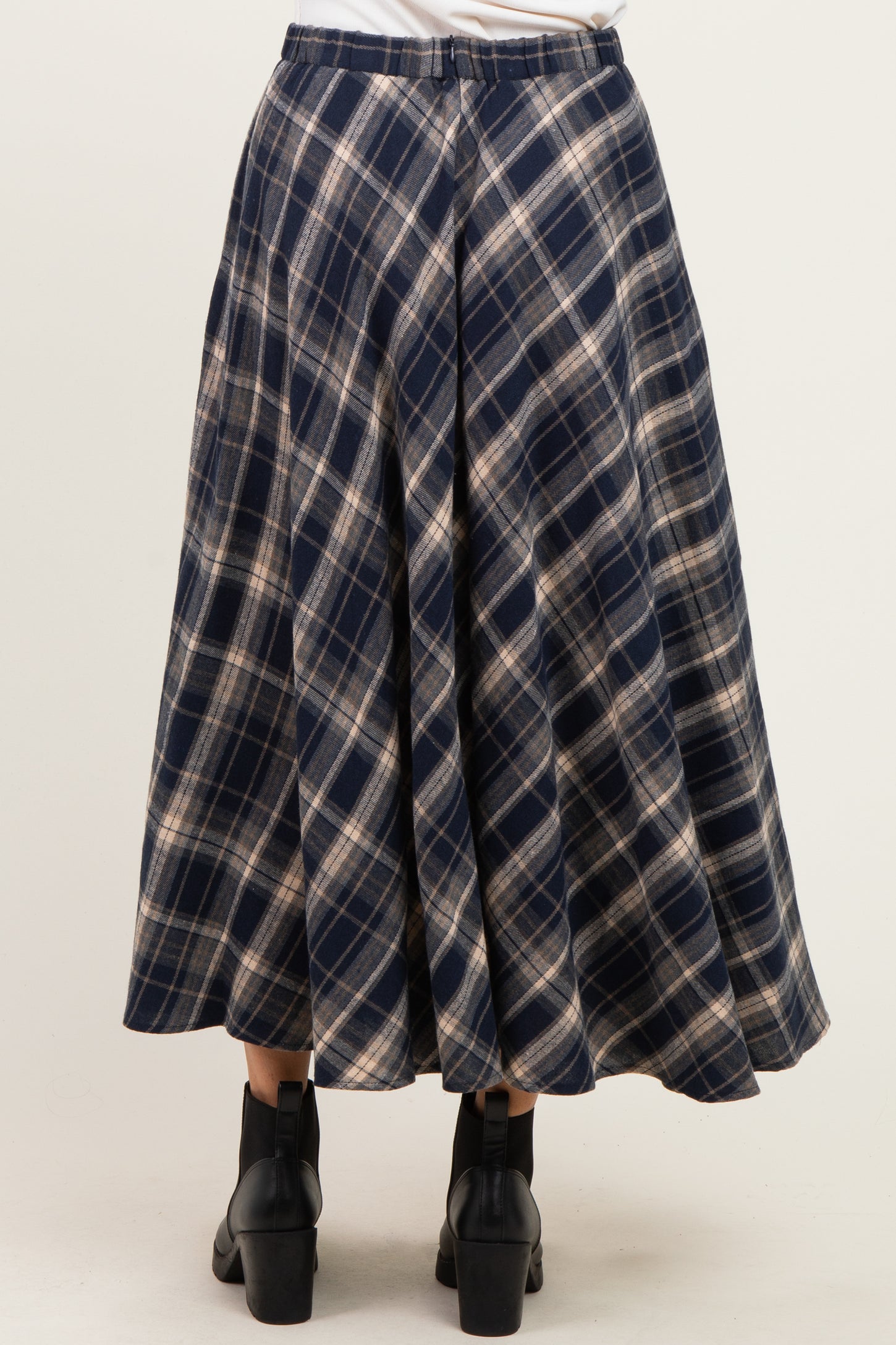 woman wearing a navy blue plaid midi skirt with pleats and black ankle boots, seen from the back