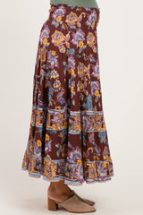 woman wearing a burgundy floral maternity maxi skirt with tiered ruffles and a smocked waistband, showing a baby bump