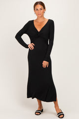 woman wearing a black long sleeve maxi dress with a twisted front detail and standing against a neutral backdrop