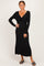 woman wearing a black long sleeve maxi dress with a twisted front detail and standing against a neutral backdrop