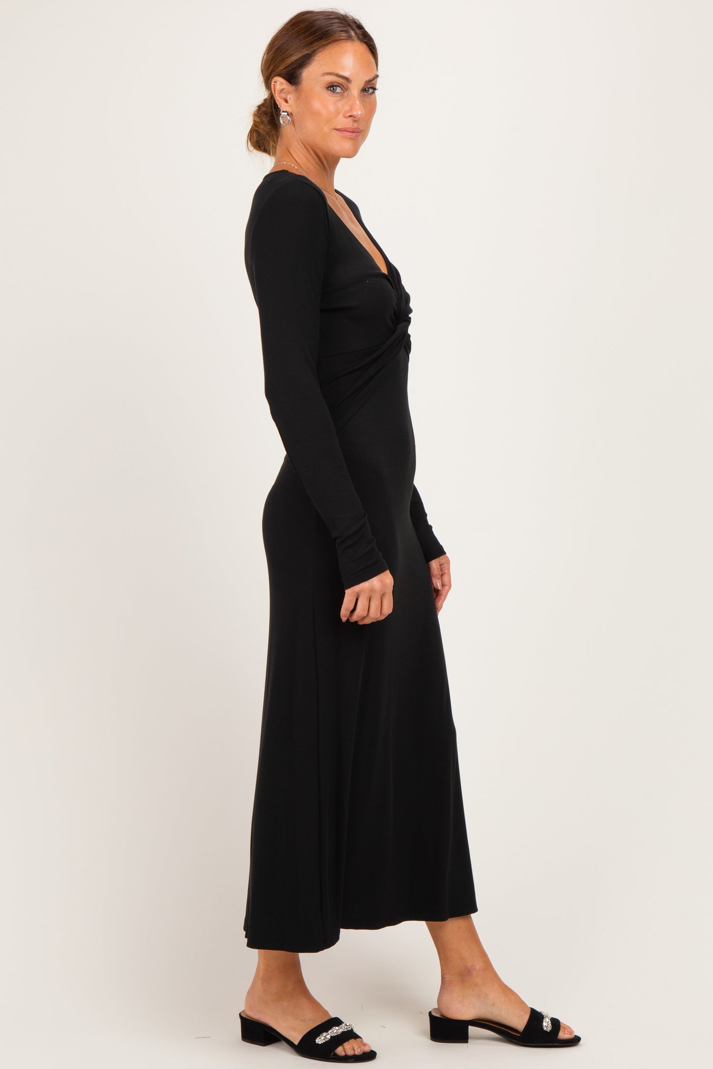 woman wearing a black long sleeve maxi dress with a twisted front detail and styled with black slide sandals