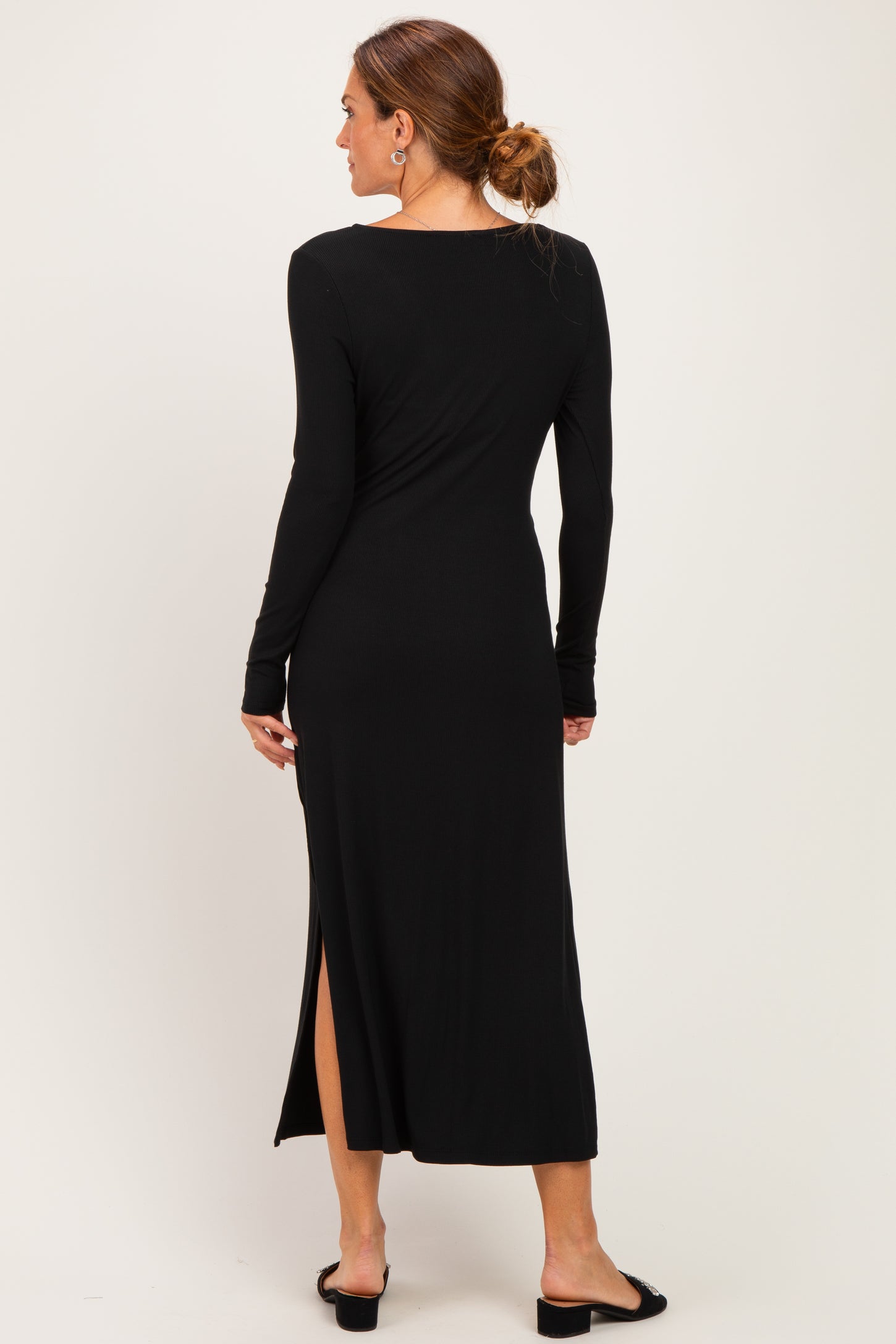 woman wearing a black long sleeve midi dress with a side slit, viewed from the back