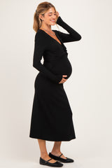 woman wearing a black long sleeve maternity dress, cradling her baby bump with a smile
