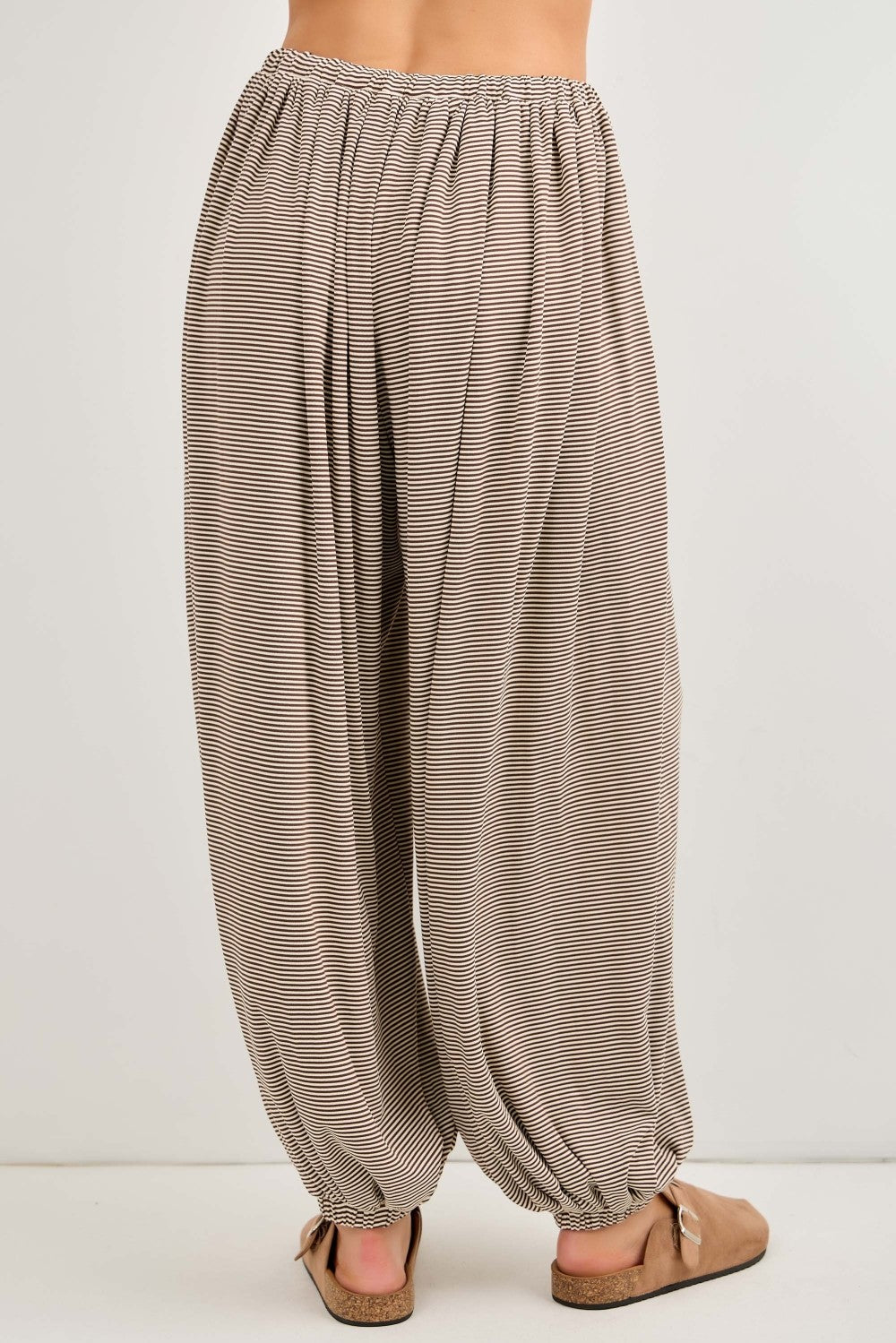 woman wearing light brown striped wide-leg pants with an elastic waistband and gathered cuffs, standing from the back