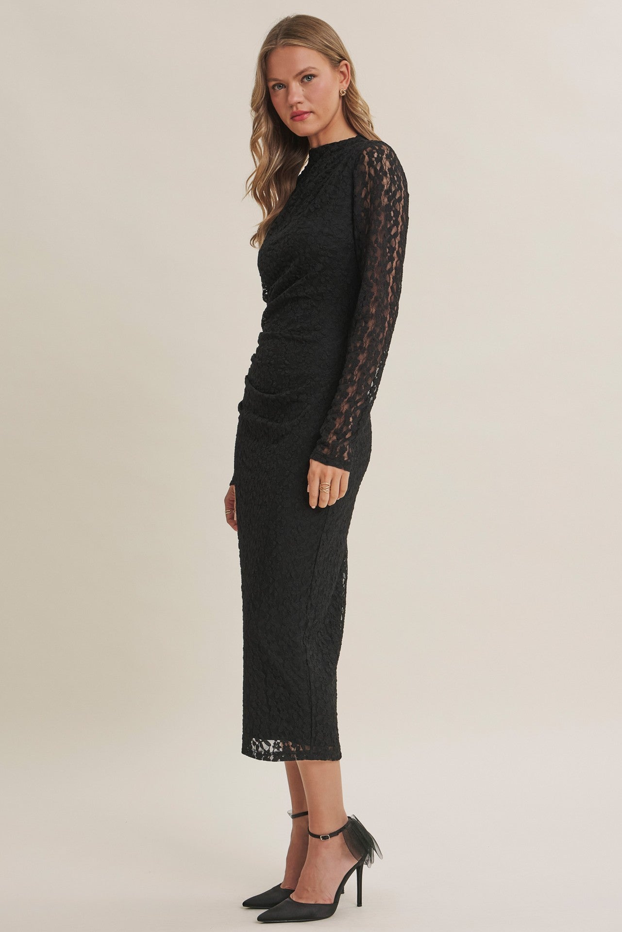 woman wearing a black lace long sleeve midi dress with a fitted silhouette and side ruching