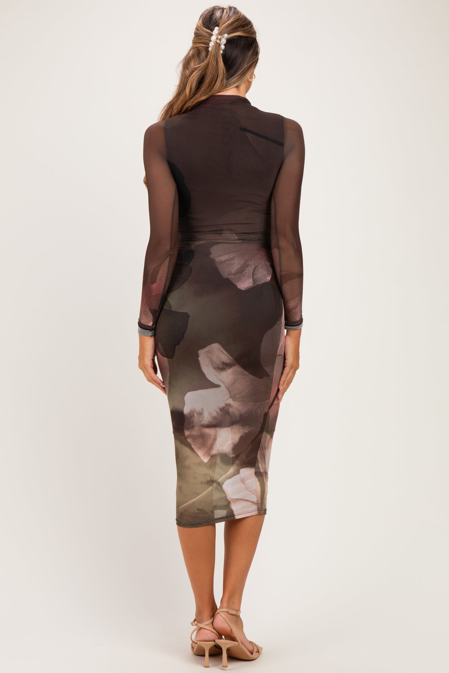 woman wearing a sheer long sleeve maternity dress with a floral print and fitted silhouette, showing a baby bump