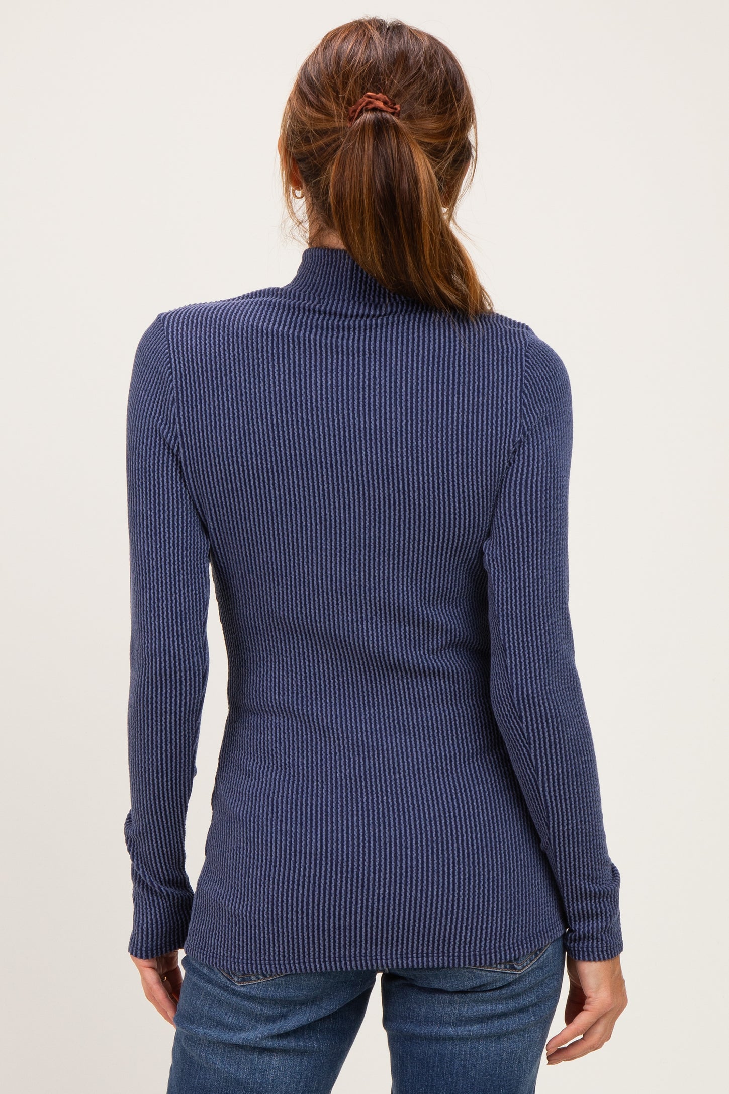 woman wearing a dark blue ribbed long sleeve top, viewed from the back with fitted silhouette and high collar