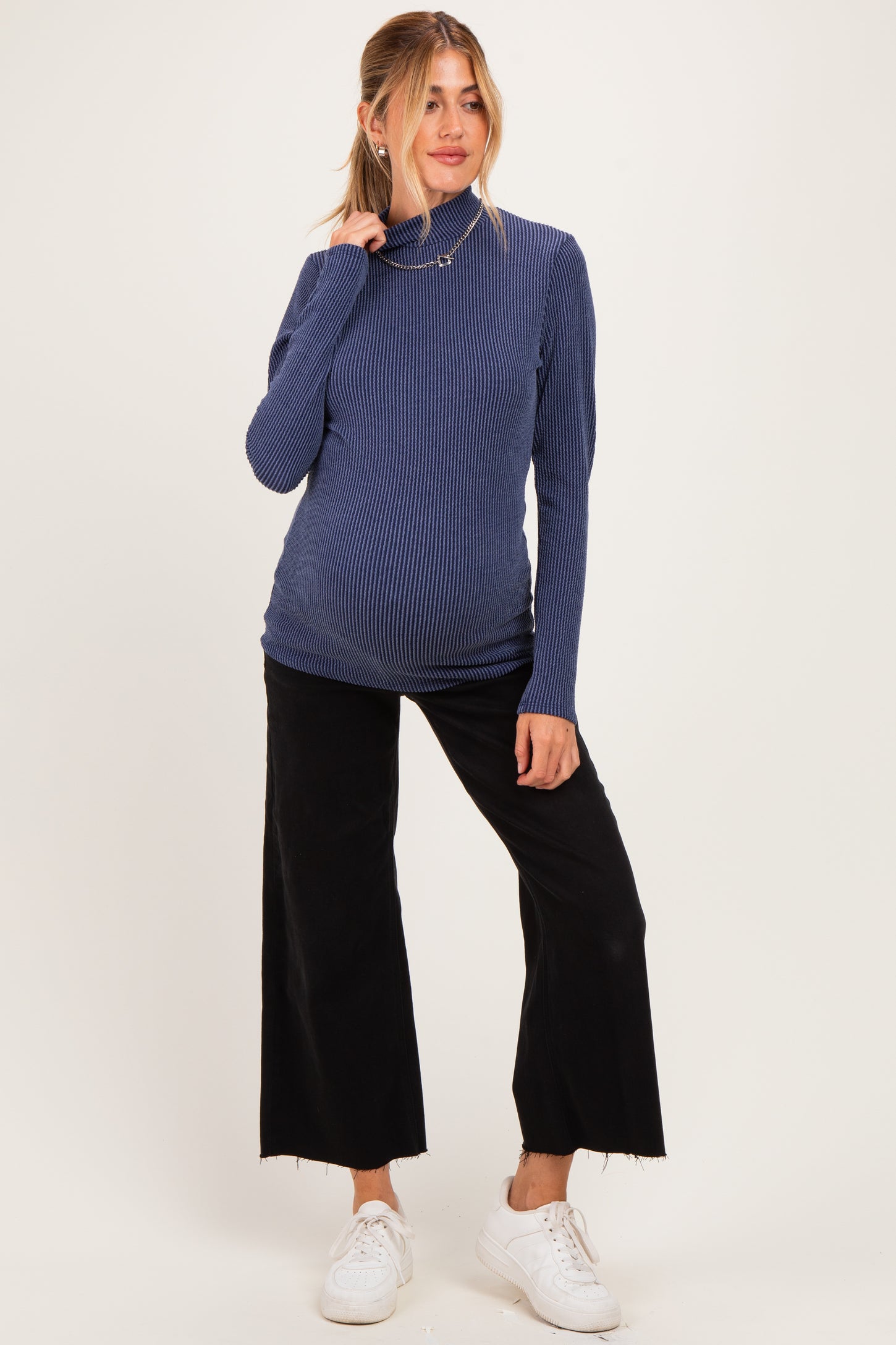 woman wearing a navy ribbed maternity turtleneck top and black wide-leg pants with a visible baby bump
