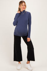 woman wearing a navy ribbed maternity turtleneck top and black wide-leg pants with a visible baby bump