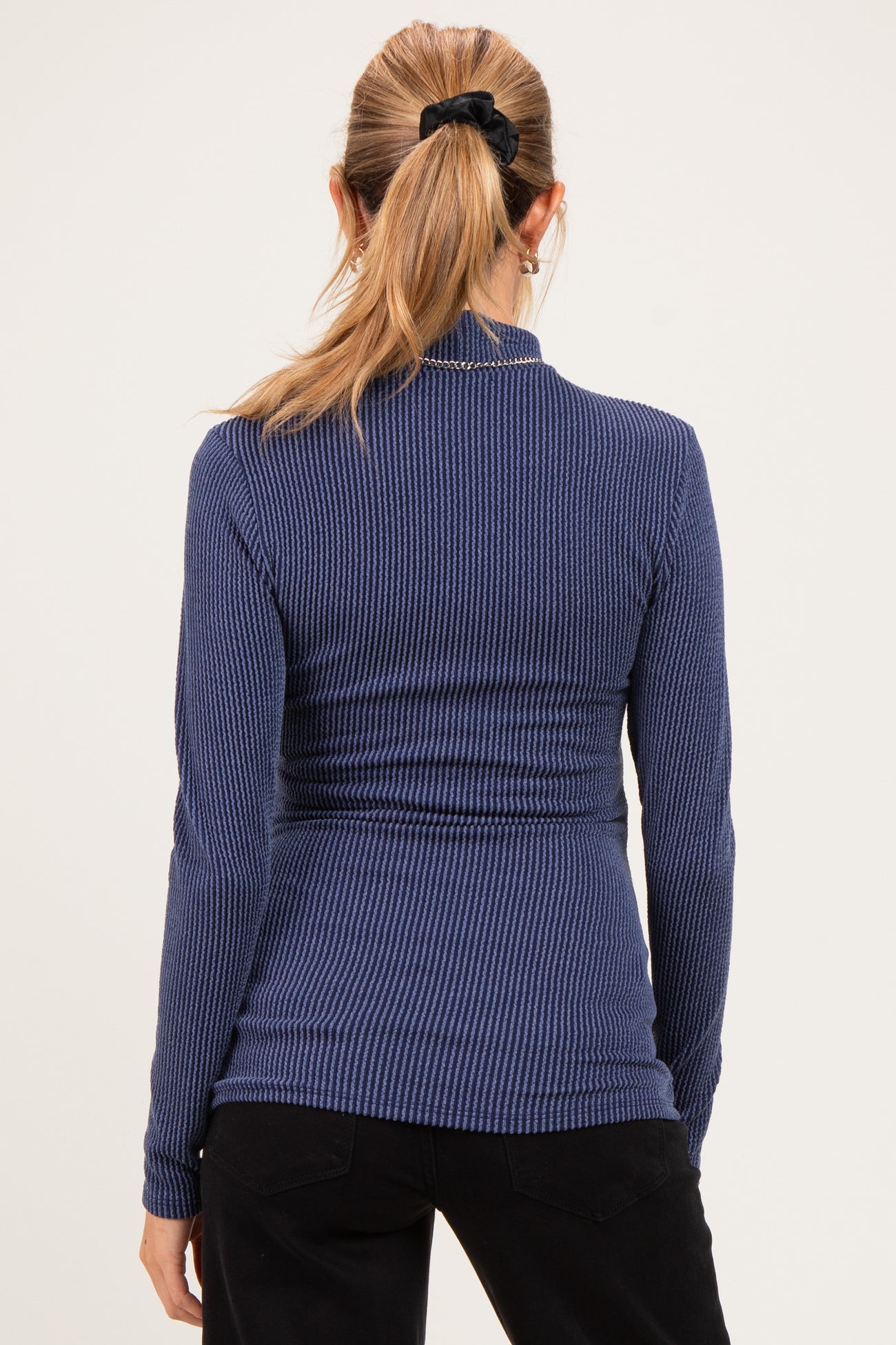 woman wearing a navy blue ribbed long sleeve maternity top, showing the back view and fitted silhouette