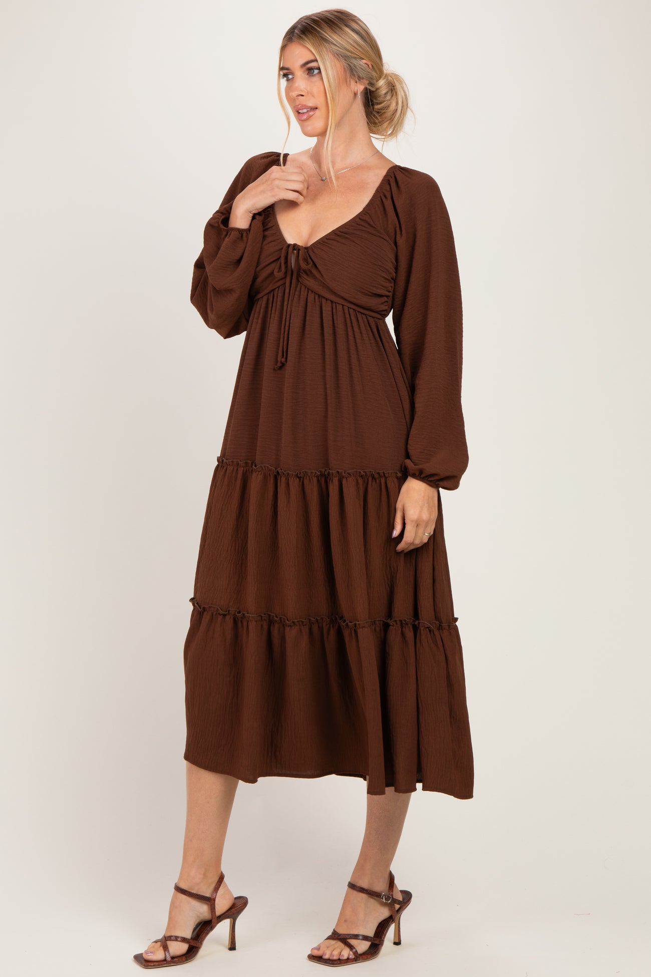 woman wearing a brown tiered midi dress with long sleeves and a gathered bodice, standing in a relaxed pose