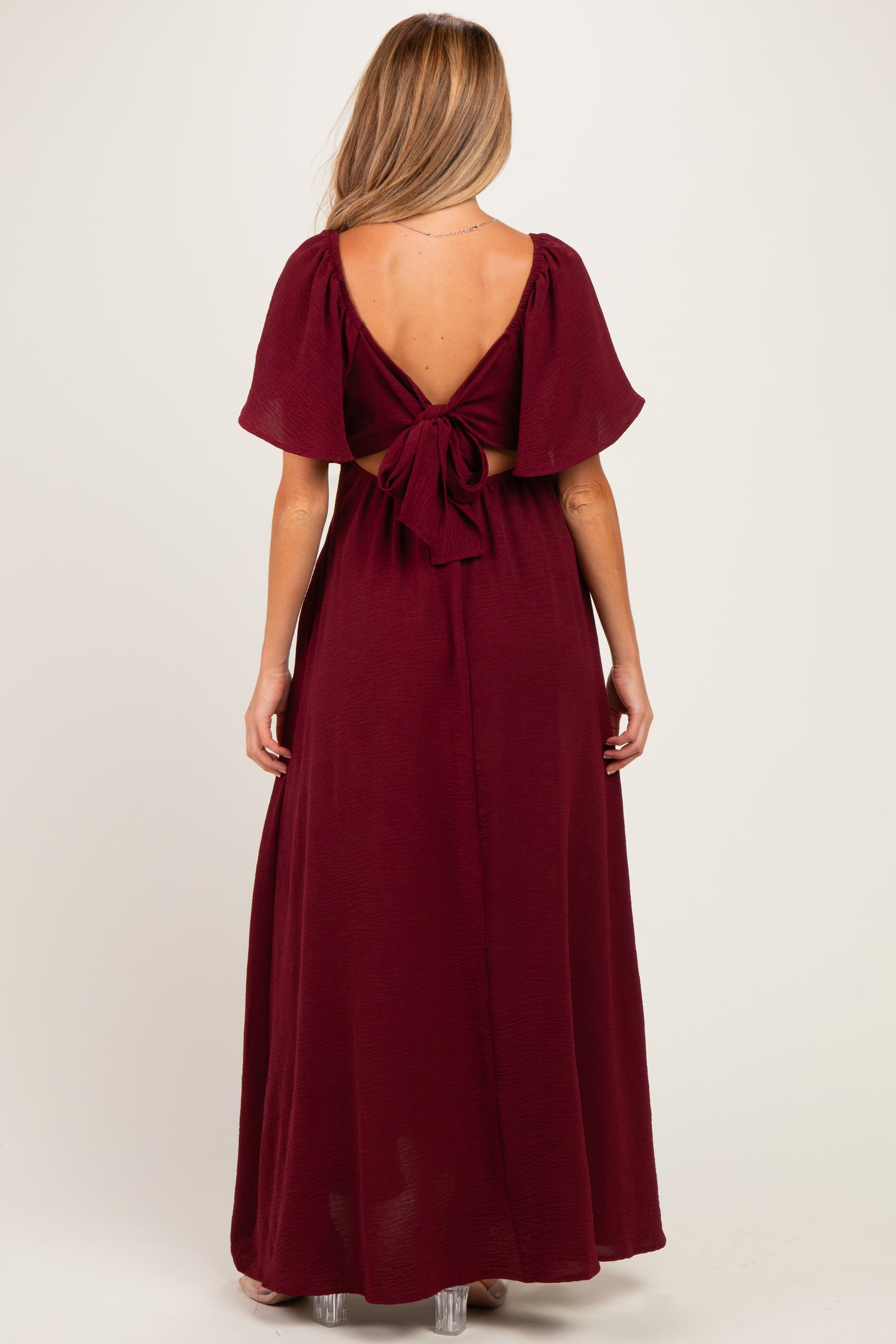 woman wearing a burgundy maternity maxi dress with short sleeves and an open back tied at the waist