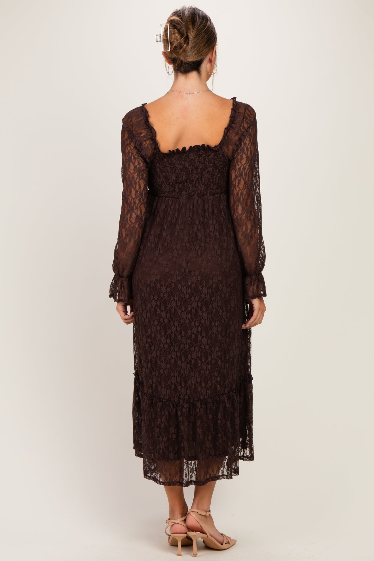 woman wearing a brown lace maternity dress with long sleeves and a ruffled hem, showing her baby bump from the back