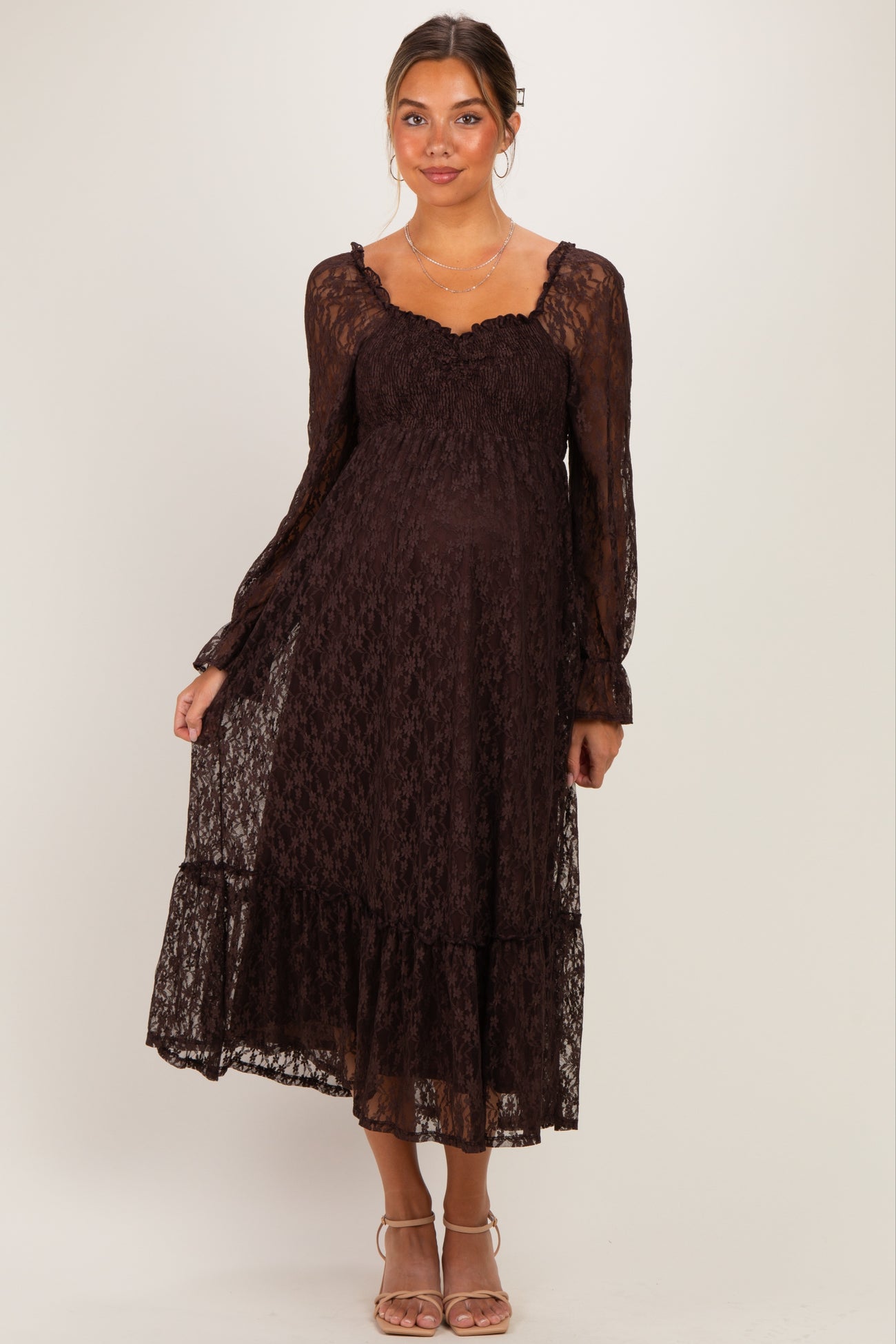 woman wearing a dark brown lace maternity dress with long sleeves and a ruffled hem, showing her baby bump