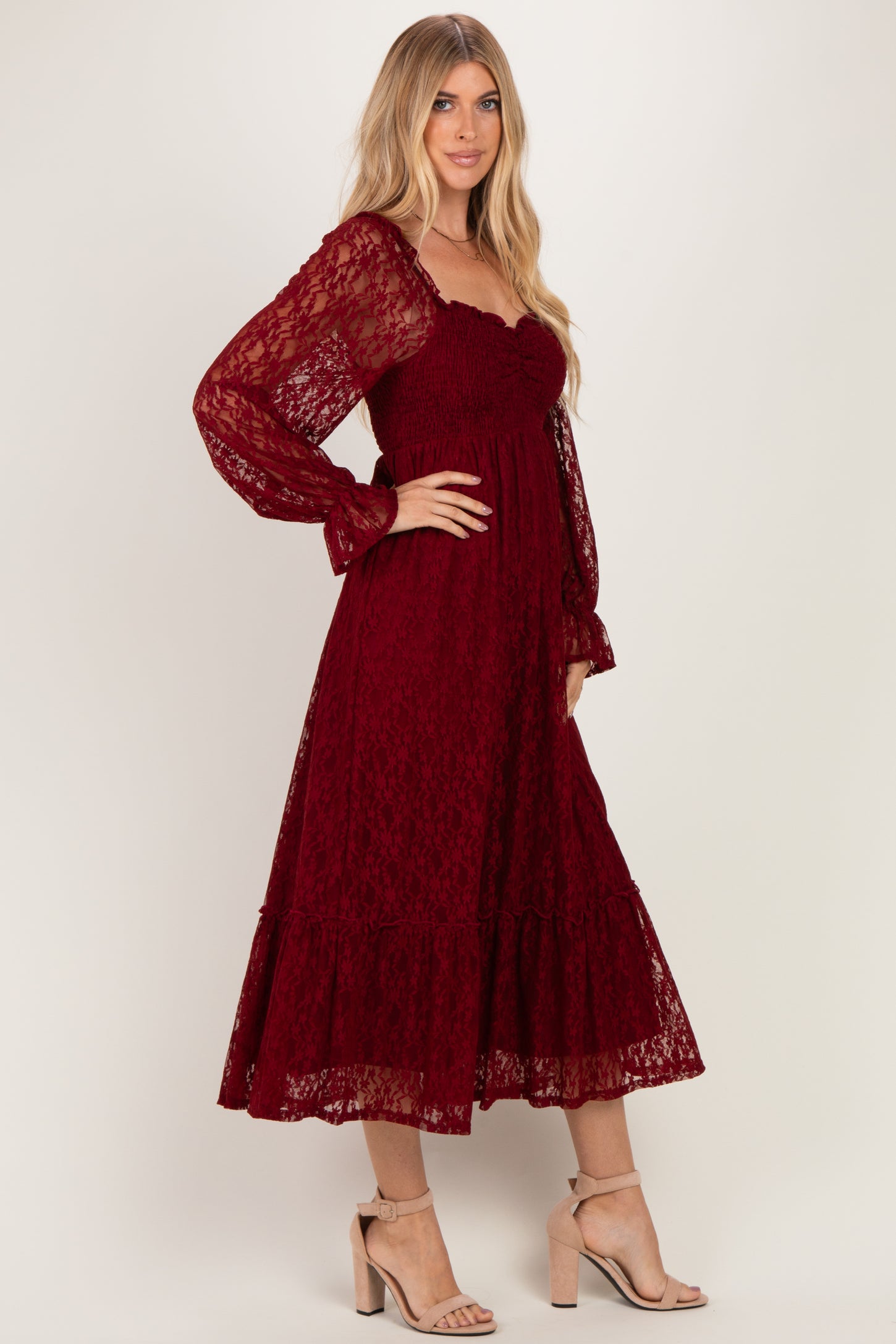 woman wearing a burgundy lace midi dress with long puff sleeves and a tiered skirt, standing in a side pose
