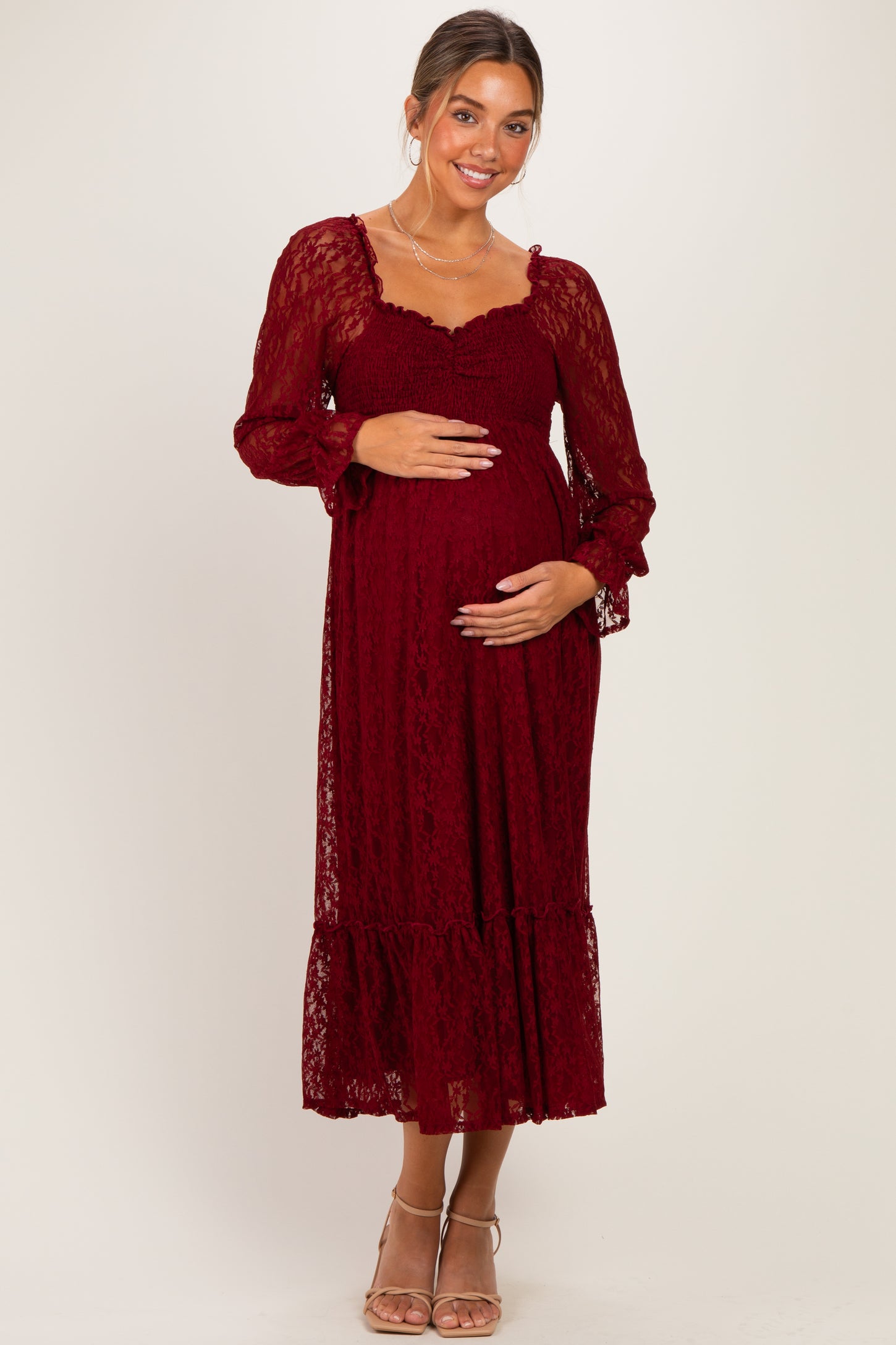 woman wearing a burgundy lace maternity dress with long sleeves and a ruffled hem, holding her baby bump