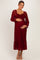 woman wearing a burgundy lace maternity dress with long sleeves and a ruffled hem, holding her baby bump