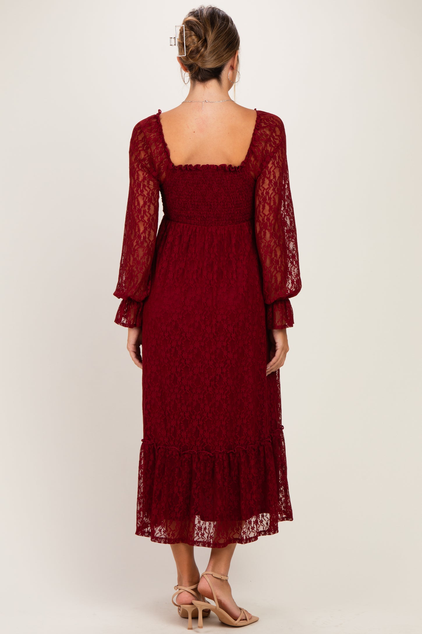 woman wearing a burgundy lace maternity dress with long sleeves and a ruffled hem, showing a partially hidden pregnant belly