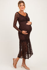 woman wearing a dark brown lace maternity dress, showcasing her baby bump, standing with one hand on her belly