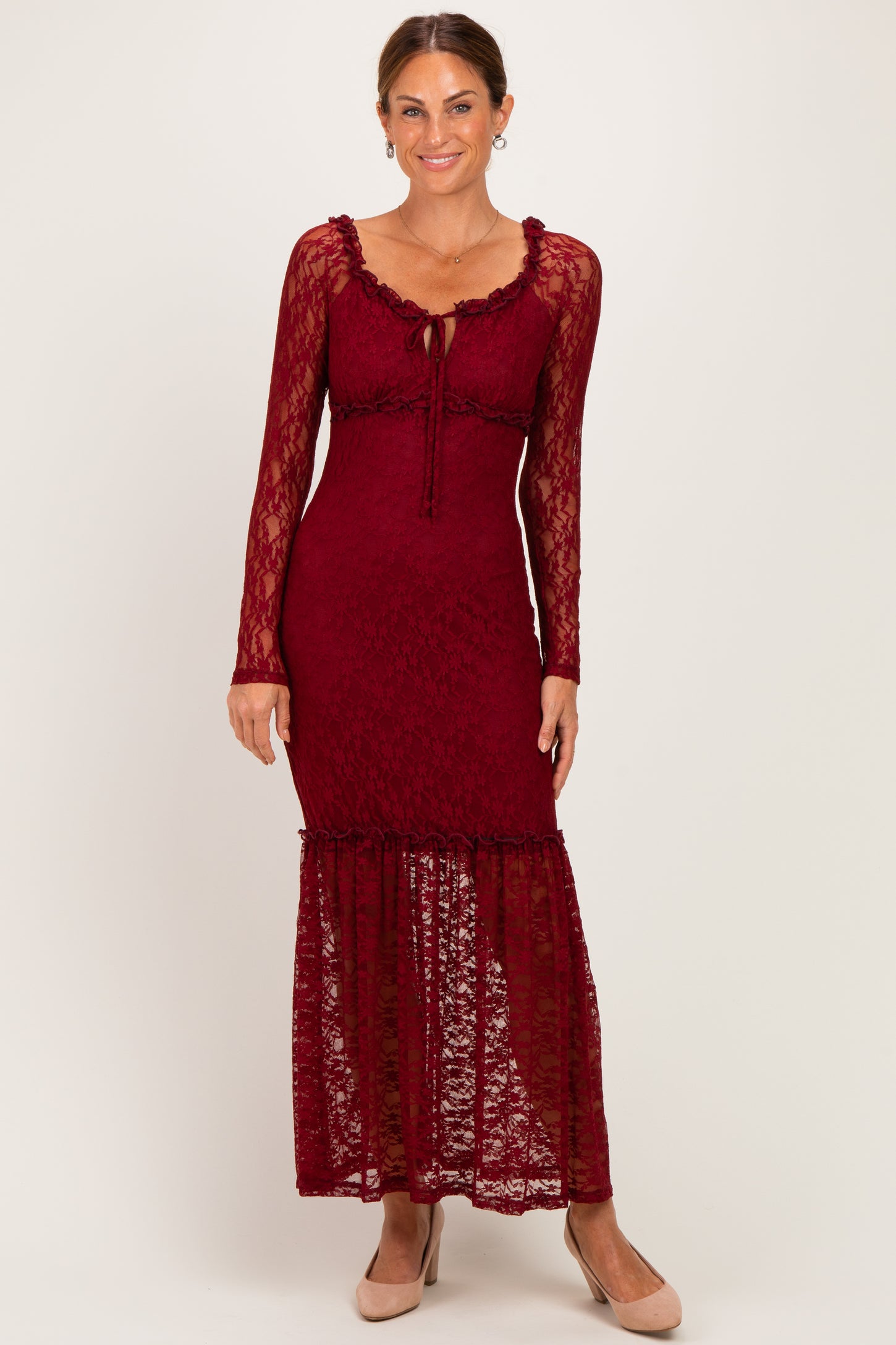 woman wearing a burgundy lace maxi dress with long sleeves and a ruffled hem, standing against a neutral background