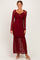 woman wearing a burgundy lace maxi dress with long sleeves and a ruffled hem, standing against a neutral background