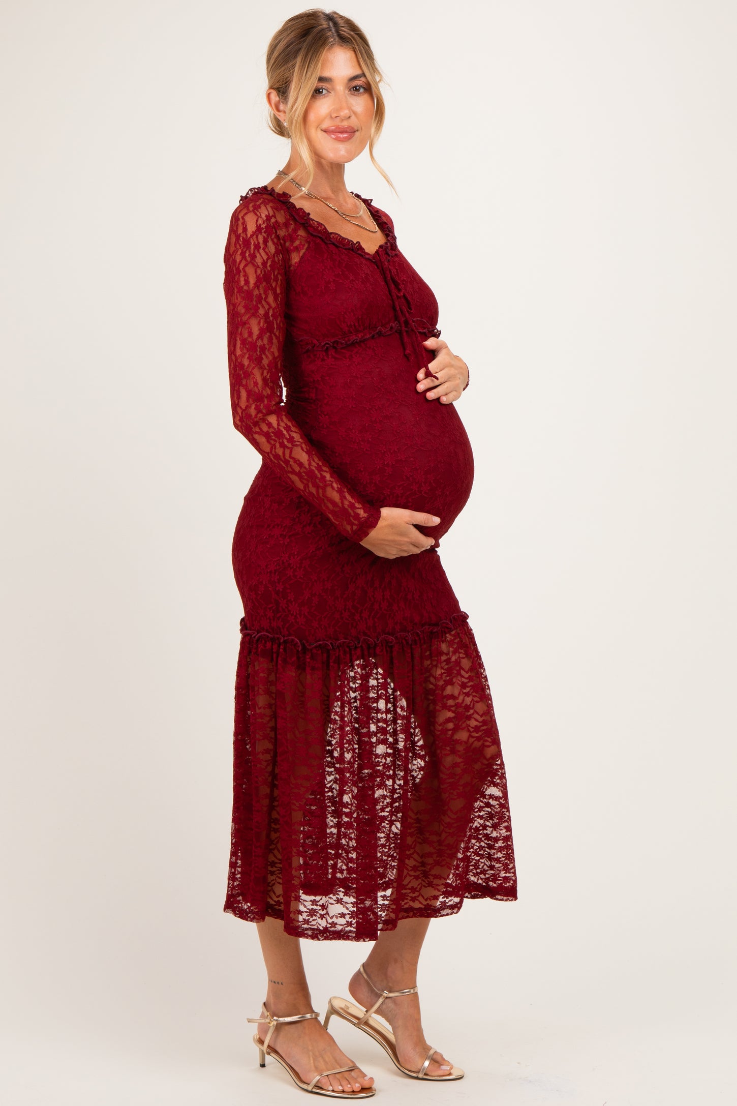 woman wearing a burgundy lace maternity dress with long sleeves and a ruffled hem, showing her baby bump