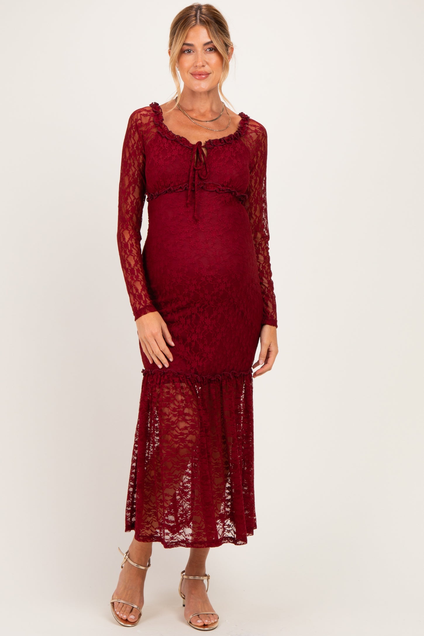 woman wearing a burgundy lace maternity dress with long sleeves and a ruffled hem, showcasing her baby bump