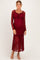 woman wearing a burgundy lace maternity dress with long sleeves and a ruffled hem, showcasing her baby bump