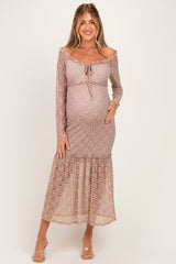 woman wearing a light brown lace maternity dress with long sleeves and a flowing hem, gently cradling her baby bump