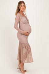 woman wearing a light brown lace maternity dress with long sleeves and a flared hem, holding her baby bump