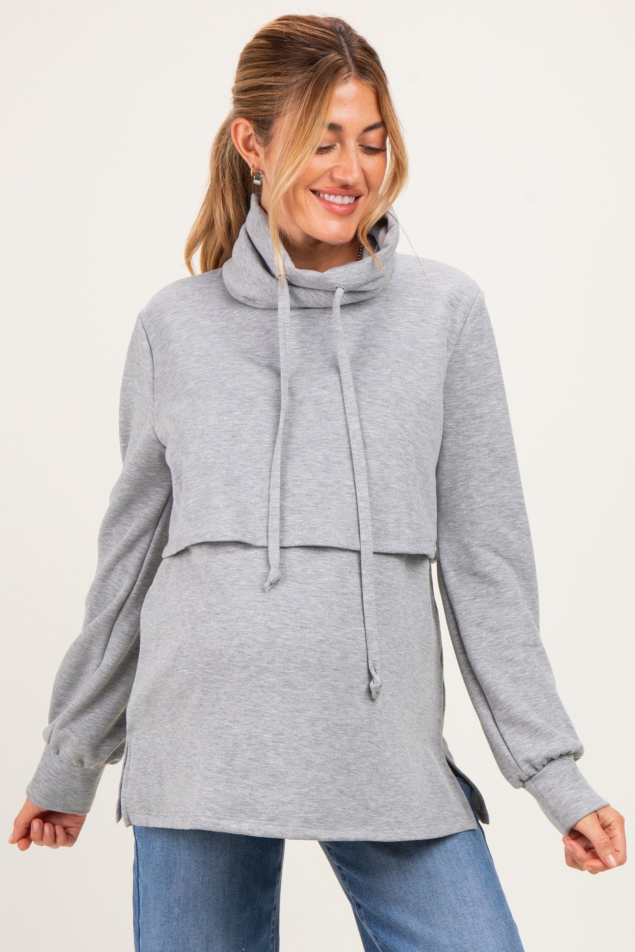 woman wearing a gray maternity pullover hoodie with a cowl neck and layered design, smiling and showing her baby bump