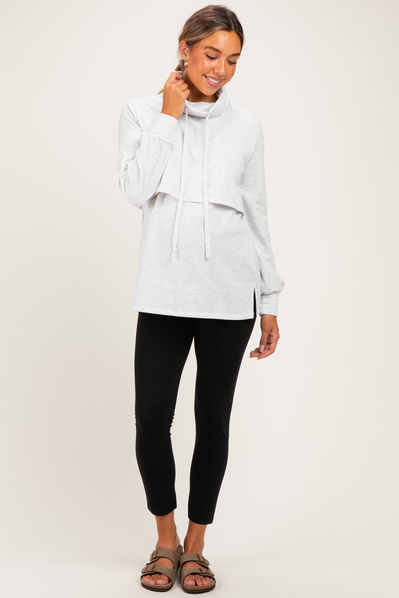 woman wearing a light gray maternity pullover hoodie with a cowl neck and side slits, paired with black leggings