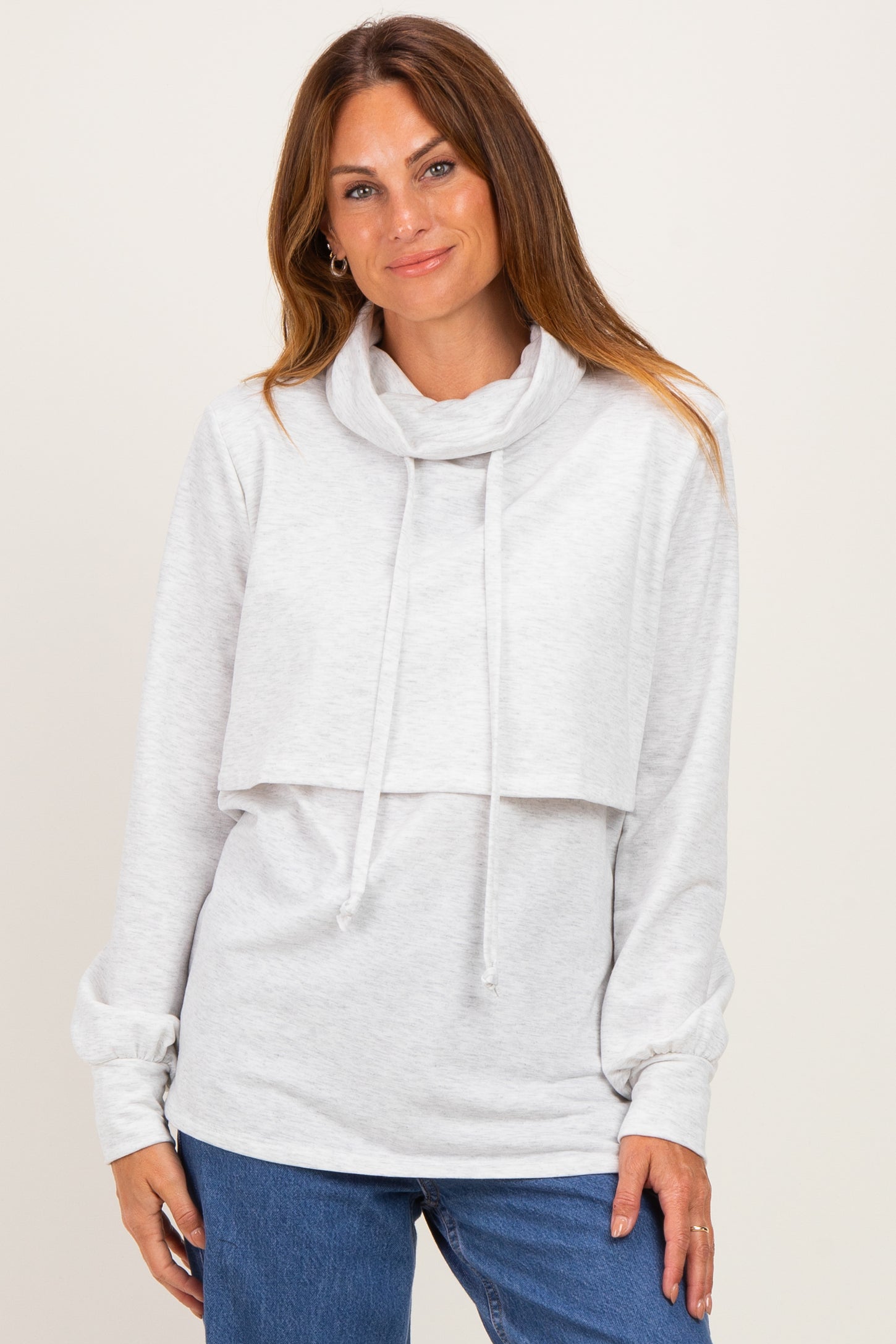 woman wearing a light gray cropped sweatshirt with a cowl neck and long sleeves paired with blue jeans