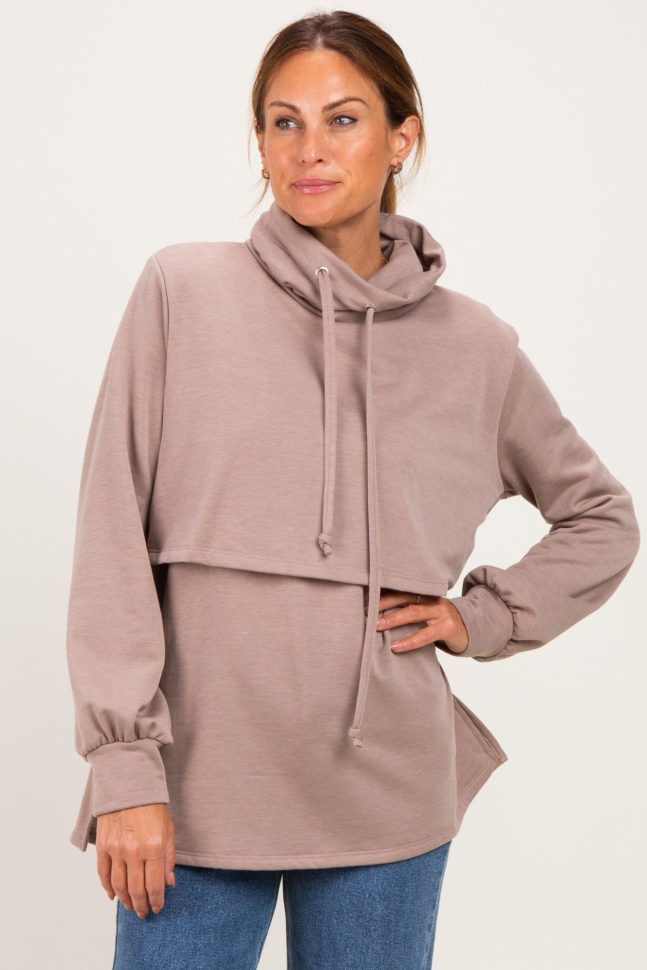 woman wearing a taupe cropped hoodie with a high neckline and side slits, styled with blue jeans