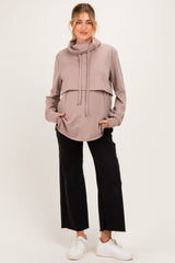 woman wearing a taupe maternity hoodie with a cowl neck and side pockets, paired with black wide-leg pants