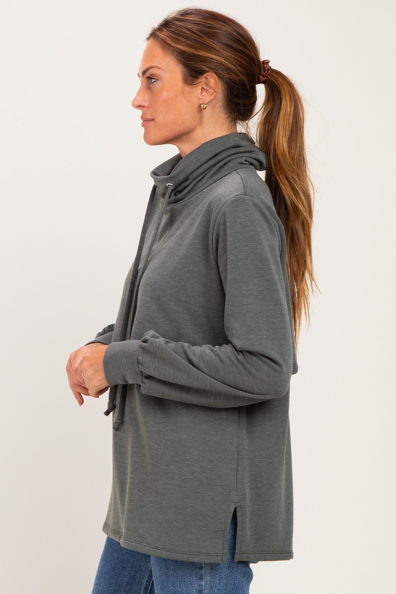 woman wearing a dark gray pullover with a high collar and side slits, styled with a ponytail