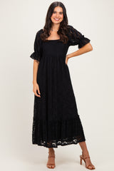 woman wearing a black lace maxi dress with flutter sleeves and a tiered hem, standing confidently and smiling