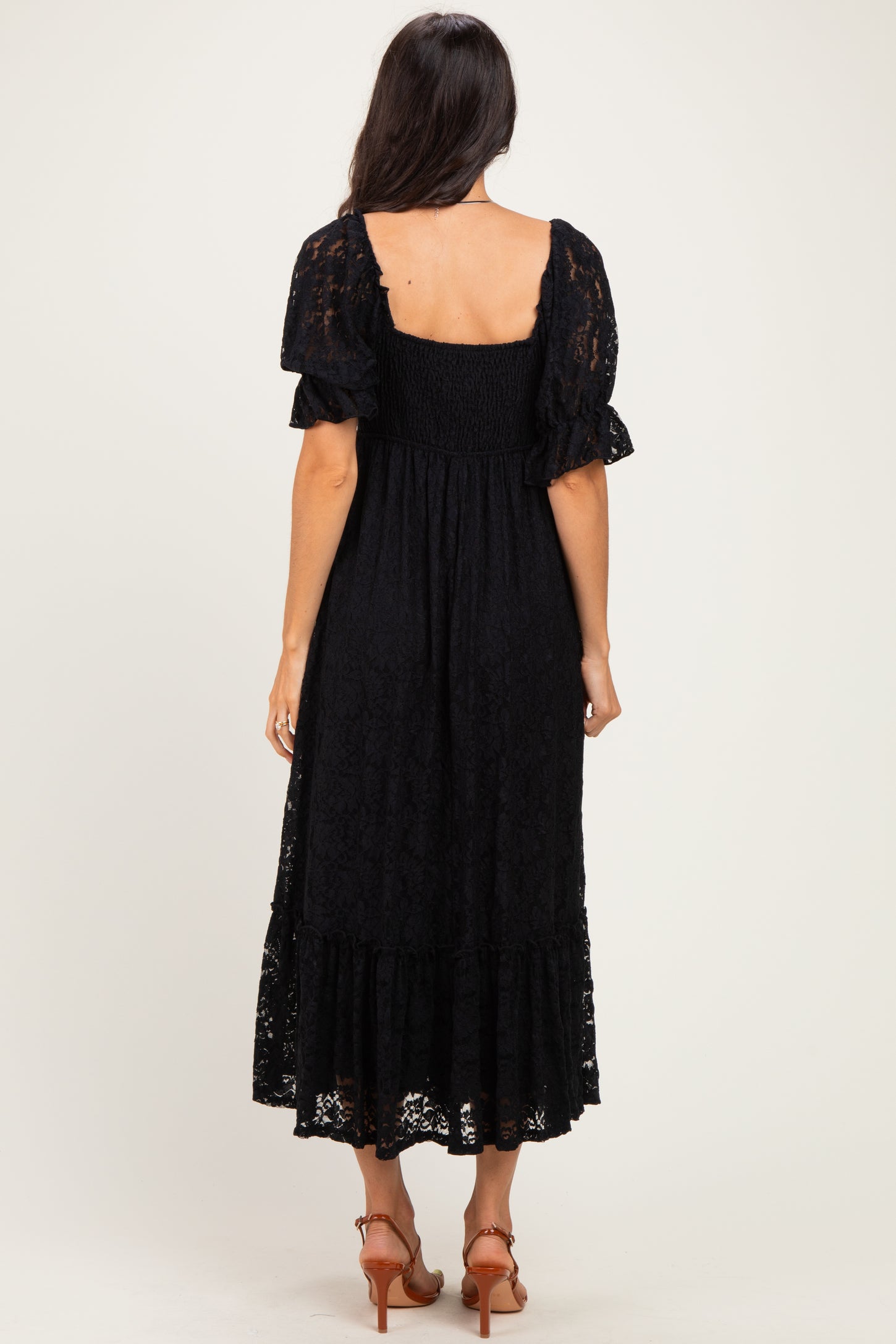 woman wearing a black lace midi dress with puff sleeves and a tiered ruffle hem, viewed from the back