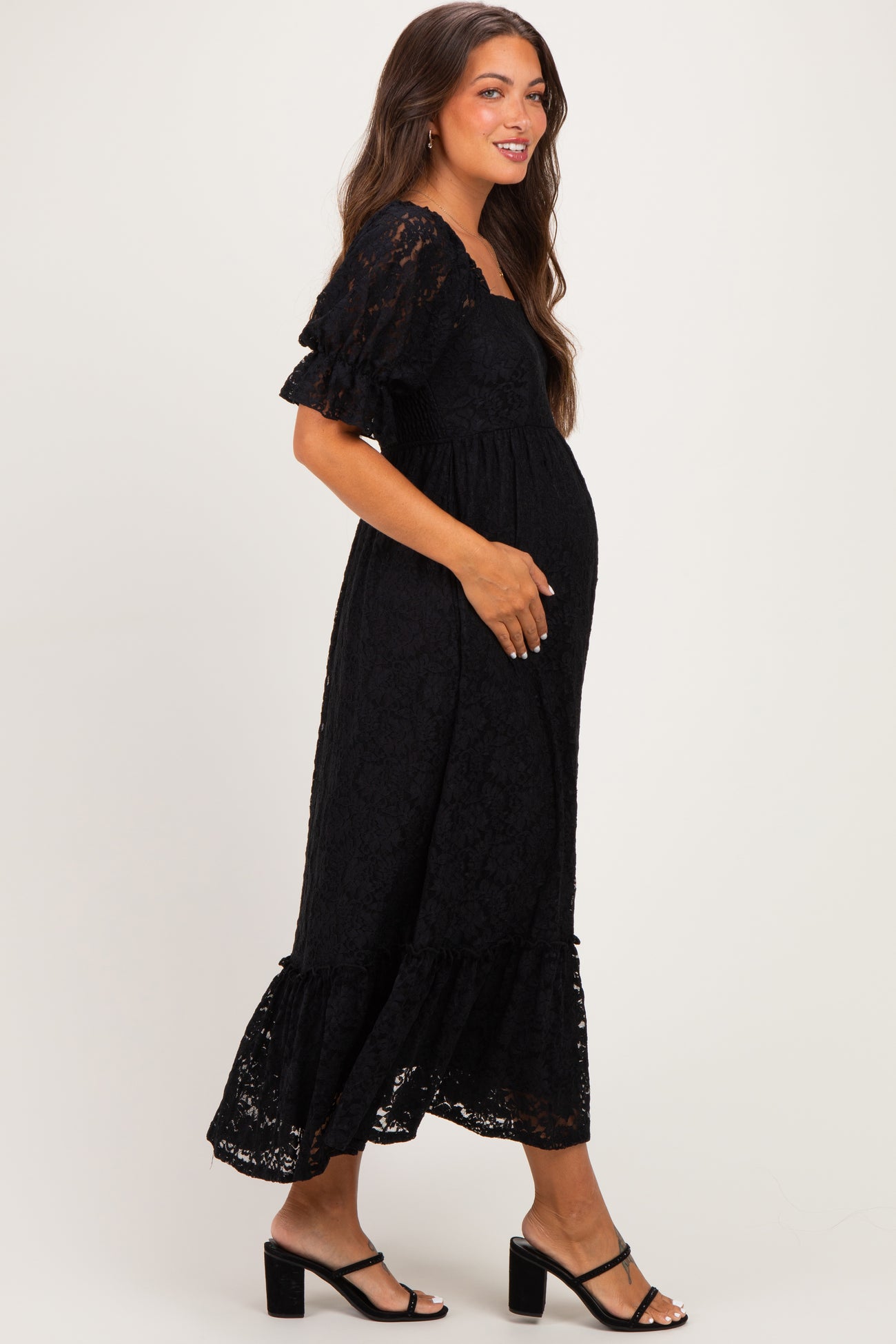 woman wearing a black lace maternity dress with short ruffled sleeves and a flowing hem, showing her baby bump