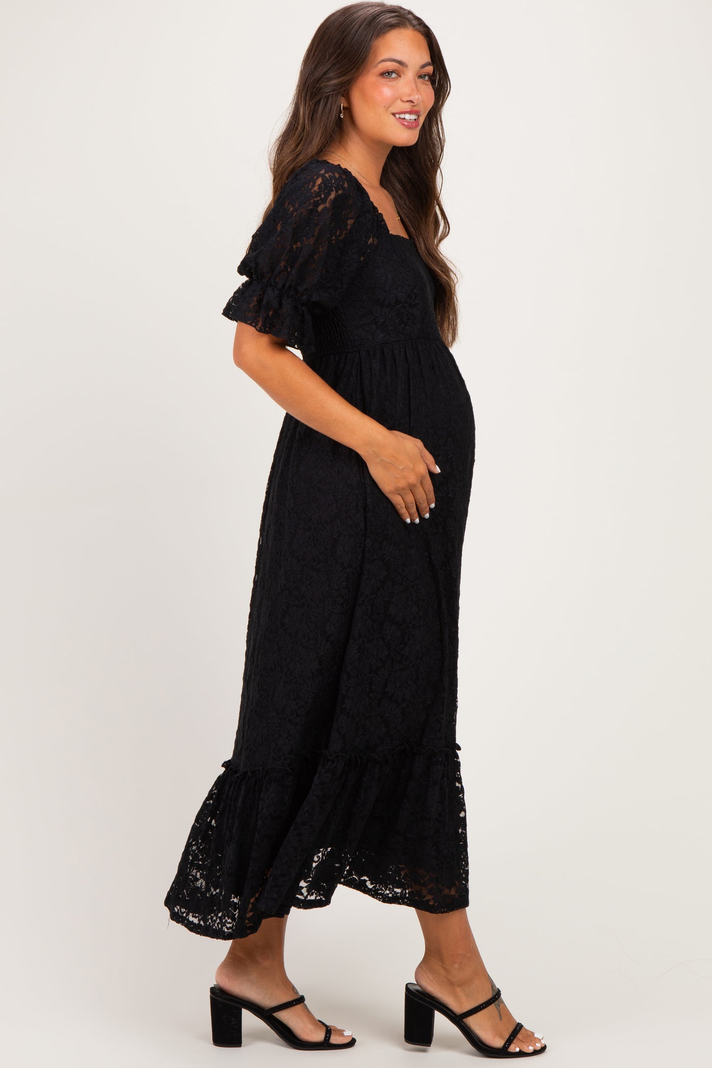 woman wearing a black lace maternity dress with short ruffled sleeves and a flowing hem, showing her baby bump
