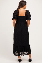 woman wearing a black lace maternity maxi dress with puff sleeves and a smocked bodice, showing a baby bump from the back