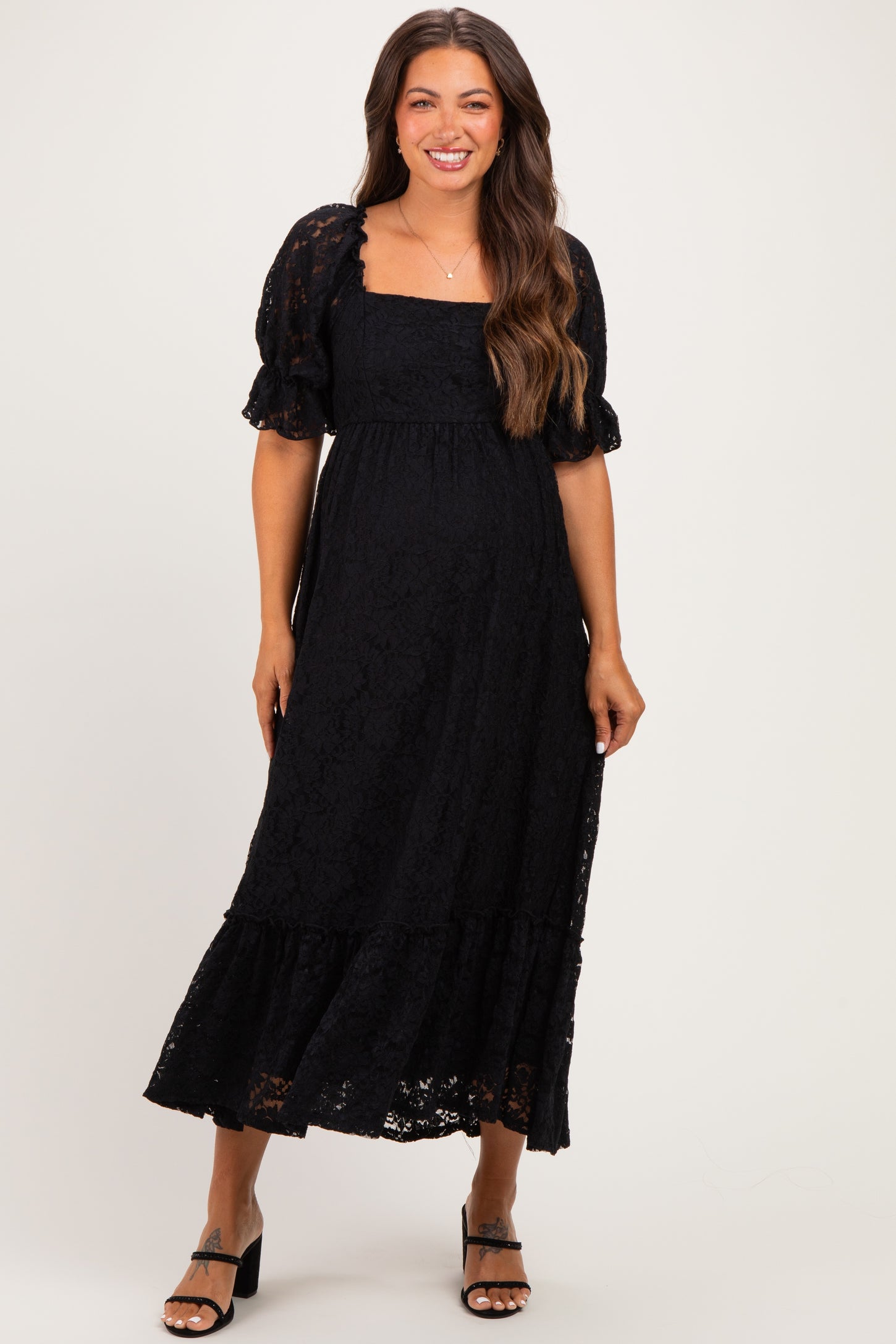 woman wearing a black lace maternity dress with puff sleeves and a tiered skirt, showing her baby bump