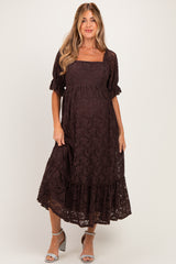 woman wearing a dark brown lace maternity dress with short sleeves and a tiered hem, standing and smiling