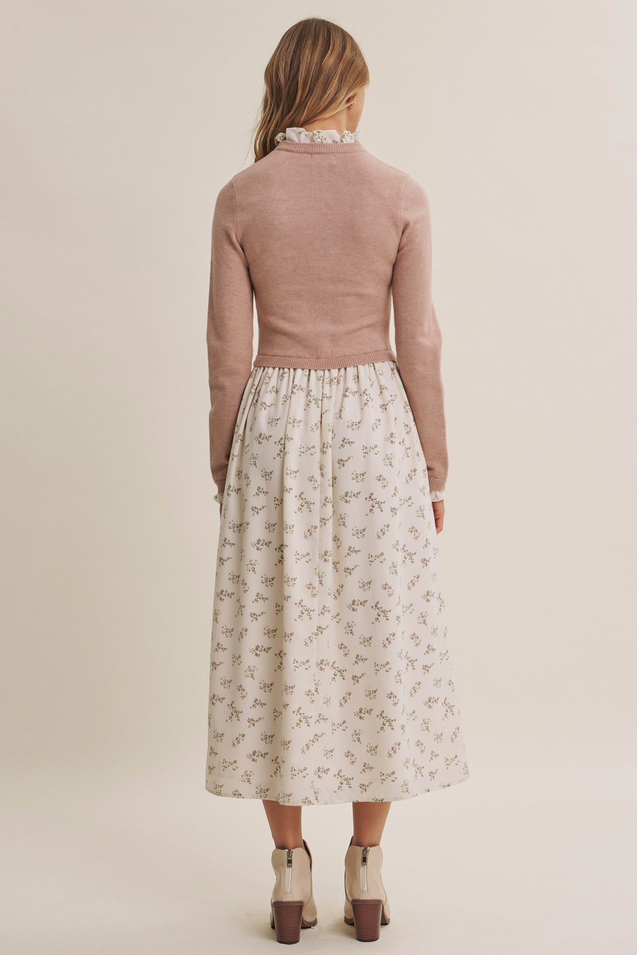 woman wearing a pink long sleeve sweater over a white floral print midi dress, viewed from the back